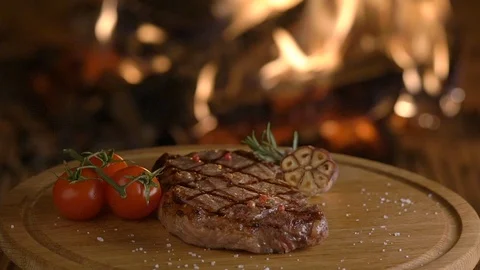 Rotating grilled beef steak on wooden board on fireplace background Stock Footage 101799671