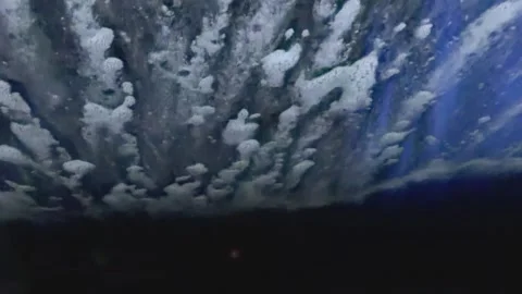 Rotating horizontal brush approaching windshield during automatic car wash throu Stock Footage 330935564