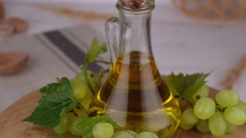 Rotating jug or bottle with grape oil against green grapes on a wooden Stock Footage 194651490