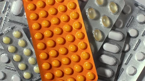 Rotating macro view of assorted pills in blister packs, orange tablets and Stock Footage 327451582