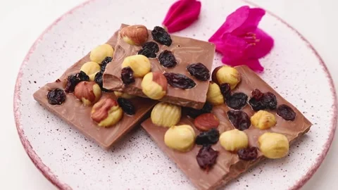 Rotating of milk chocolate with hazelnuts and raisins on ceramic plate on white. Stock Footage 133725612