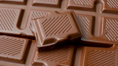 Rotating milk chocolate square piece resting on textured chocolate bar close up Stock Footage 344865173