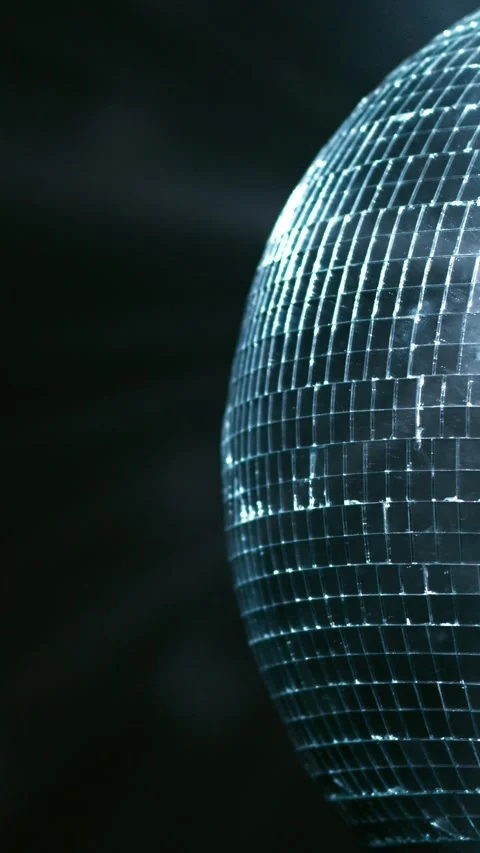 Rotating mirrored disco ball reflecting blue light against a dark background in Stock Footage 347734761