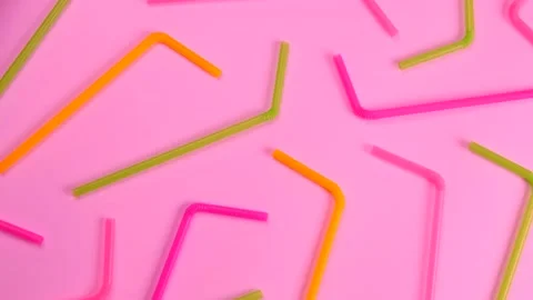 Rotating multi-colored cocktail straws on a pink background, Stock Footage 220015514