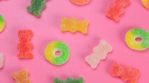Rotating multi-colored gummy bears and rings on a pink background, the concept Stock Footage 198565427