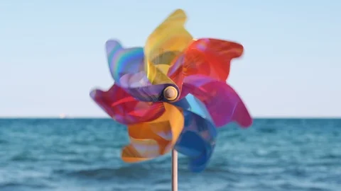 A rotating multi-colored plastic pinwheel with a blowing wind stands  sand sea Stock Footage 105688419