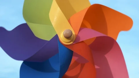 A rotating multi-colored plastic pinwheel a blowing wind stands on the blue sky. Video stock 108563597