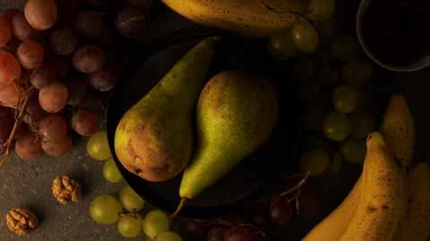 Rotating pears on brown plate with grapes bananas coffee beans and walnuts Stock Footage 320567167