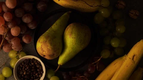 Rotating pears on brown plate with grapes bananas coffee beans and walnuts Stock Footage 320568975