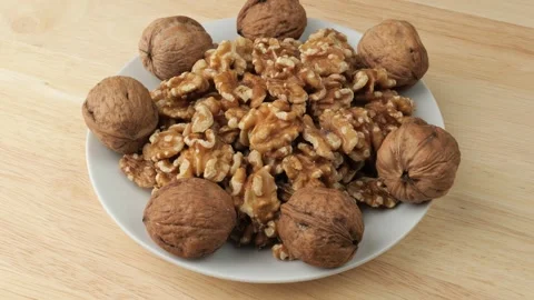 Rotating plate of walnuts with shells on wooden table Stock Footage 348309017