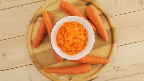 Rotating raw grated carrot with whole carrots on a cutting board Stock Footage 337011604