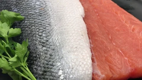 Rotating raw salmon fillet with its pink meat, silver skin, and green parsley Stock-Footage 79854304