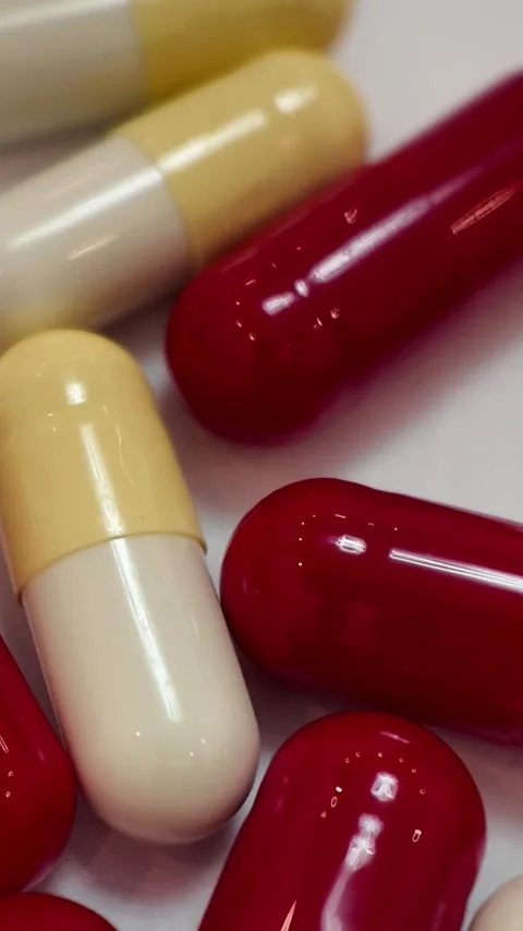 Rotating red and beige pharmaceutical capsules macro video - Vertical Version Stock Footage 345164370