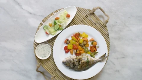 Rotating roasted sea bream fish with vegetables, sauce, and fresh salad Stock-Footage 122235625