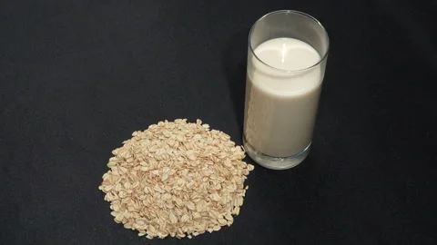 Rotating Rolled Oats and Fresh Glass of Milk on Black Background. Видео 333050658