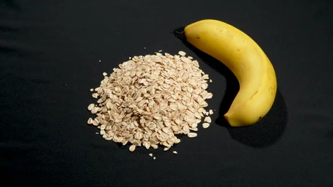 Rotating Rolled Oats and Fresh Banana on Black Background. Video stock 333092194