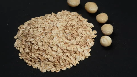 Rotating Rolled Oats and Premium Macadamia Nuts on Black Background. Видео 333051460