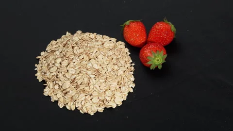 Rotating Rolled Oats and Three Fresh Strawberries on Black Background. Stockbeeldmateriaal 333091207