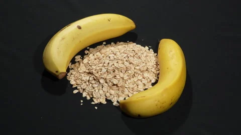 Rotating Rolled Oats with Two Fresh Bananas on Black Background. Video stock 333093591