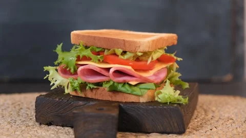 Rotating sandwich with ham cheese and fresh vegetables on dark background Vídeos de archivo 332788862