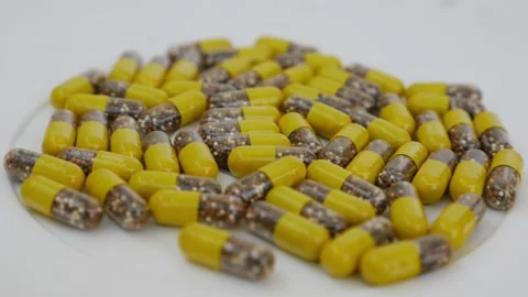 Rotating shot of capsules placed over a white table, Yello0w and brown granul Stock Footage 147700176