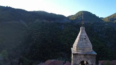 Rotating Shot of Old Stone Bell Tower with Cross over Mountain Ridge at Sunrise 스톡 동영상 324867601