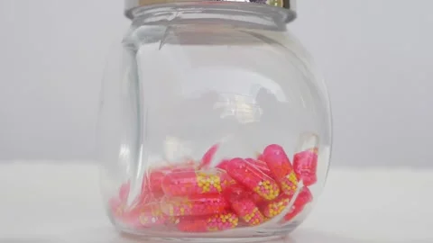 Rotating shot of pink tablets in a transparent glass bottle Stock Footage 147700162