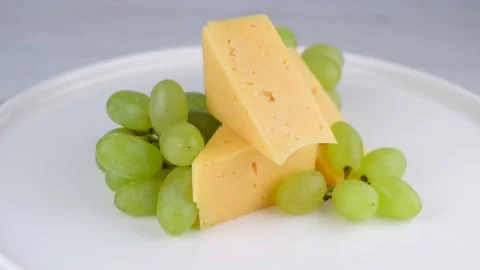Rotating slices of cheese with grapes on a white plate or background close-up Stock Footage 198138852