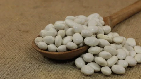 Rotating a spoon, overflowing with haricot beans, lying on burlap. Stock Footage 86600449