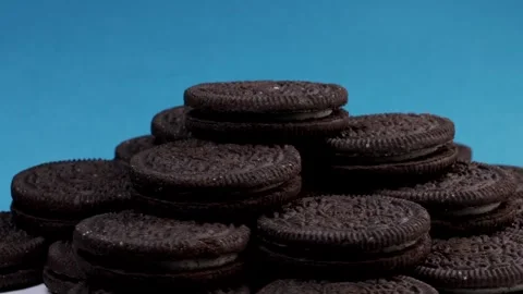 Rotating stack of chocolate sandwich cookies with cream filling on blue Stock Footage 304323783