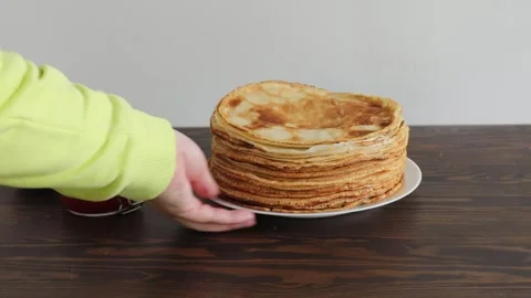 Rotating stack of golden crepes on white plate over dark wooden table with plain Stock Footage 309301776