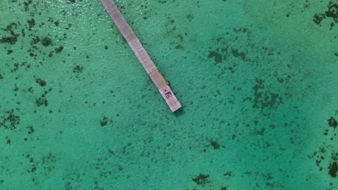 Rotating Top-Down Aerial View of Couple Lying on Wooden Pier in Emerald Ocean Wa Vídeos de archivo 345992022