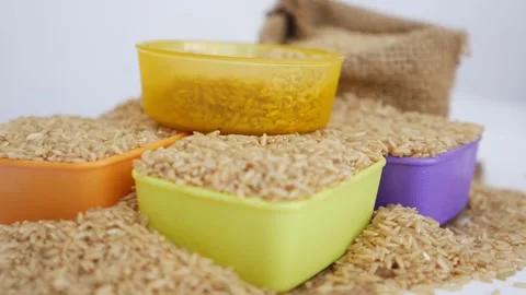 Rotating view of plastic bowls placed over heap of brown rice Stock Footage 147690334