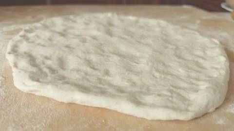 Rotating view of a raw pizza dough or focaccia on a wooden surface, close-up. Stock Footage 329037658