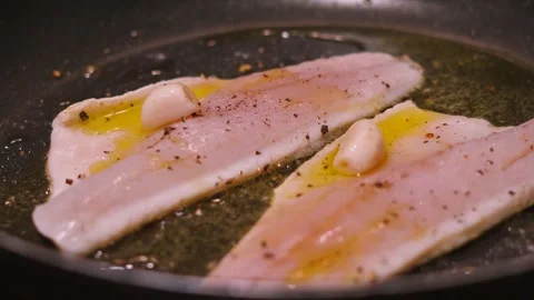 Rotating view of two sea bass fillets in a hot pan cooking skin side down in Stock Footage 333994068
