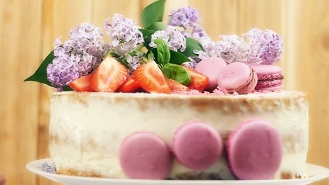 Rotating wedding cake decorated with purple macaroons, sliced strawberries and Video stock 99373693