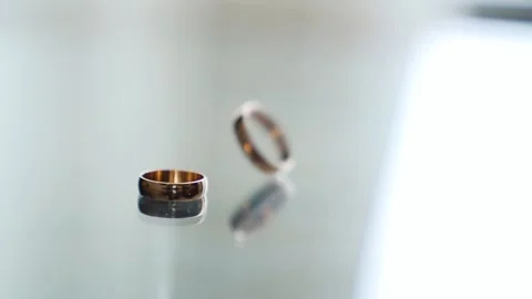 Rotating wedding gold ring in slow motion on the white mirror table Video stock 205894490