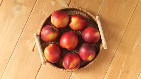 Rotating wicker basket of fresh nectarines on a wooden table Stock Footage 337441372