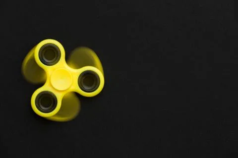 Rotating yellow fidget spinner device on black background.. Top view. Playing Stock Photos