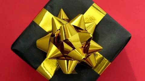 Rotation of black gift box with gold ribbon on red background. Black Friday Stock Footage 215832557