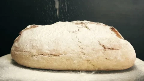 Rotation of dark bread with cracks. From above pours flour in slow motion. Stock Footage 89617882