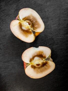 Rotten inside of an apple, cut in half and resting on top of dark cutting board. Stock Photos