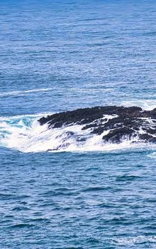 Rough blue ocean waves crash against dark volcanic rocks with white sea foam Stock Photos