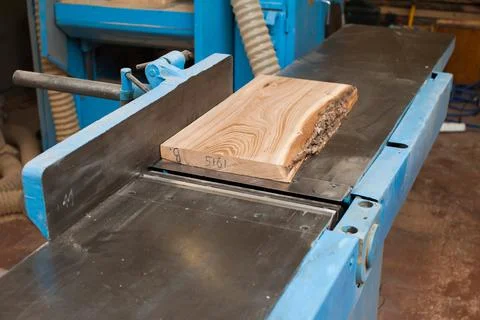 A rough board lies on a large jointer in a carpentry shop. Manufacturing of w Stock Photos