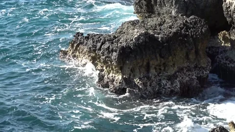 Rough dark coastal rock with white sea foam at the waterline Stockbeeldmateriaal 342394061
