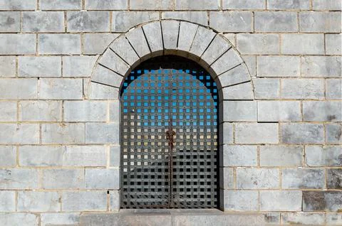 Rough gray old stone wall with grey iron gate closed with chain and padlock Stock-Fotos