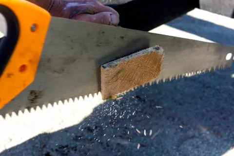 Rough hands of builder are sawing a wooden board with hacksaw 库存照片