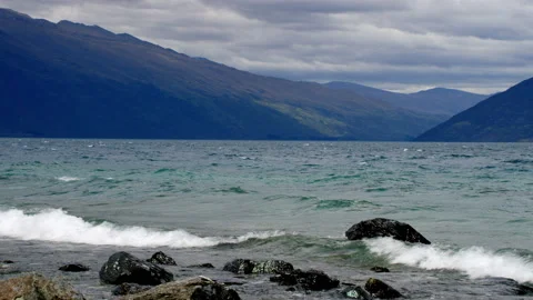 Rough lake with breaking waves and mountains with dark sky Stock Footage 159748338