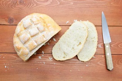 Rough loaf of bread, a slice of bread and a knife. On a wooden brown backgrou Stock Photos