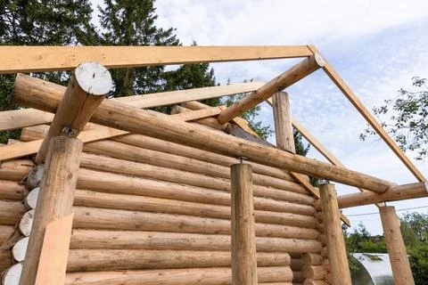 Rough log cabin under construction features wall of stacked logs and timber.. Stock Photos